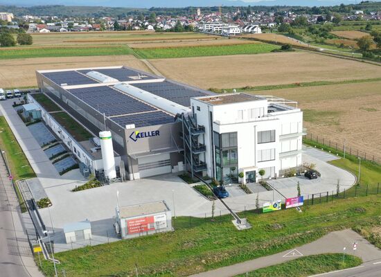 Luftbild eines mit Photovoltaikmodulen bestückten Firmengebäudes am Rand einer Ortschaft