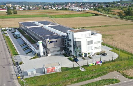 Luftbild eines mit Photovoltaikmodulen bestückten Firmengebäudes am Rand einer Ortschaft